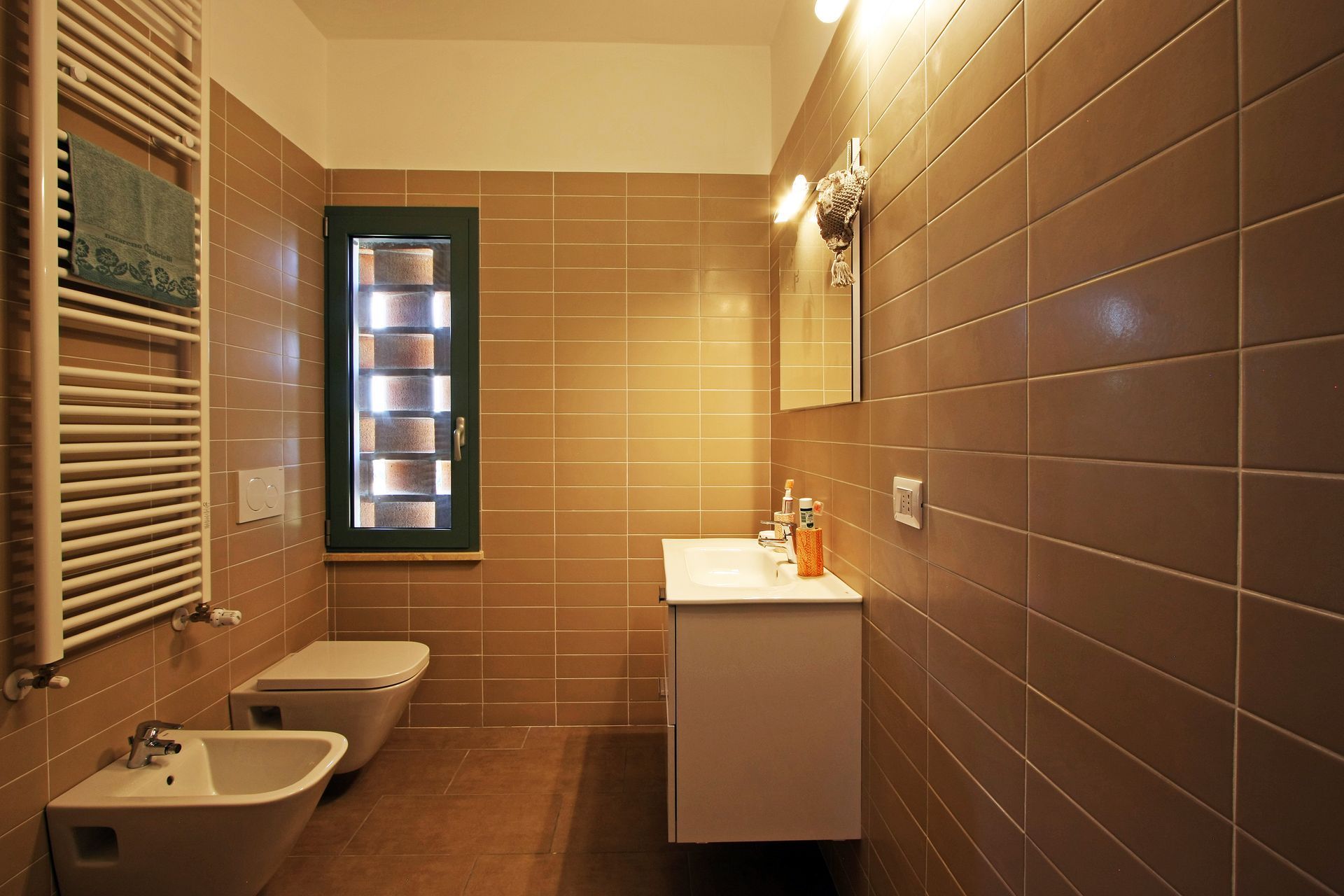 Un bagno moderno con pareti rivestite di piastrelle beige, un mobile lavabo bianco, un bidet, un WC,