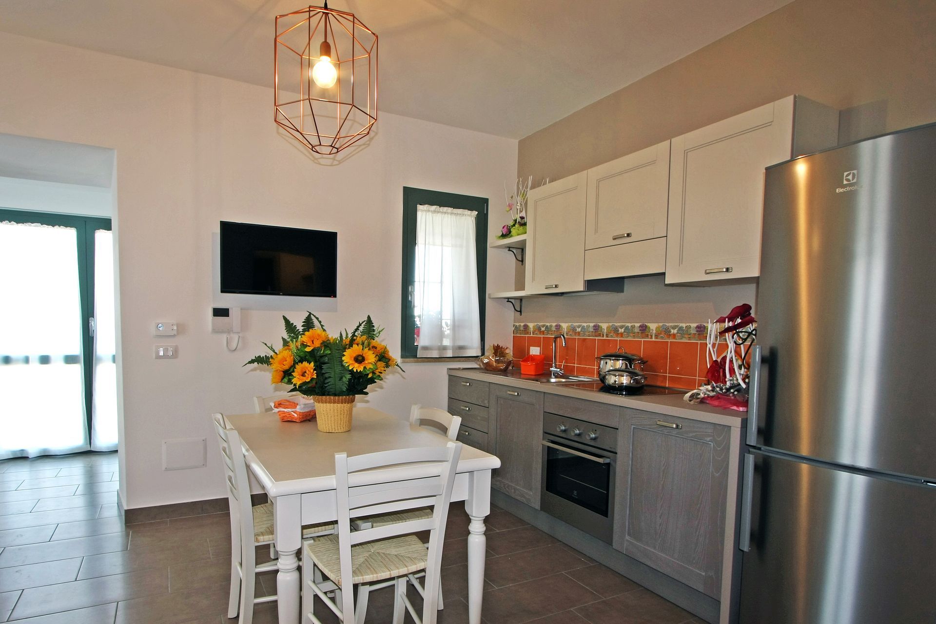 Una cucina con zona pranzo, arredata con un tavolo bianco decorato con girasoli, un frigorifero