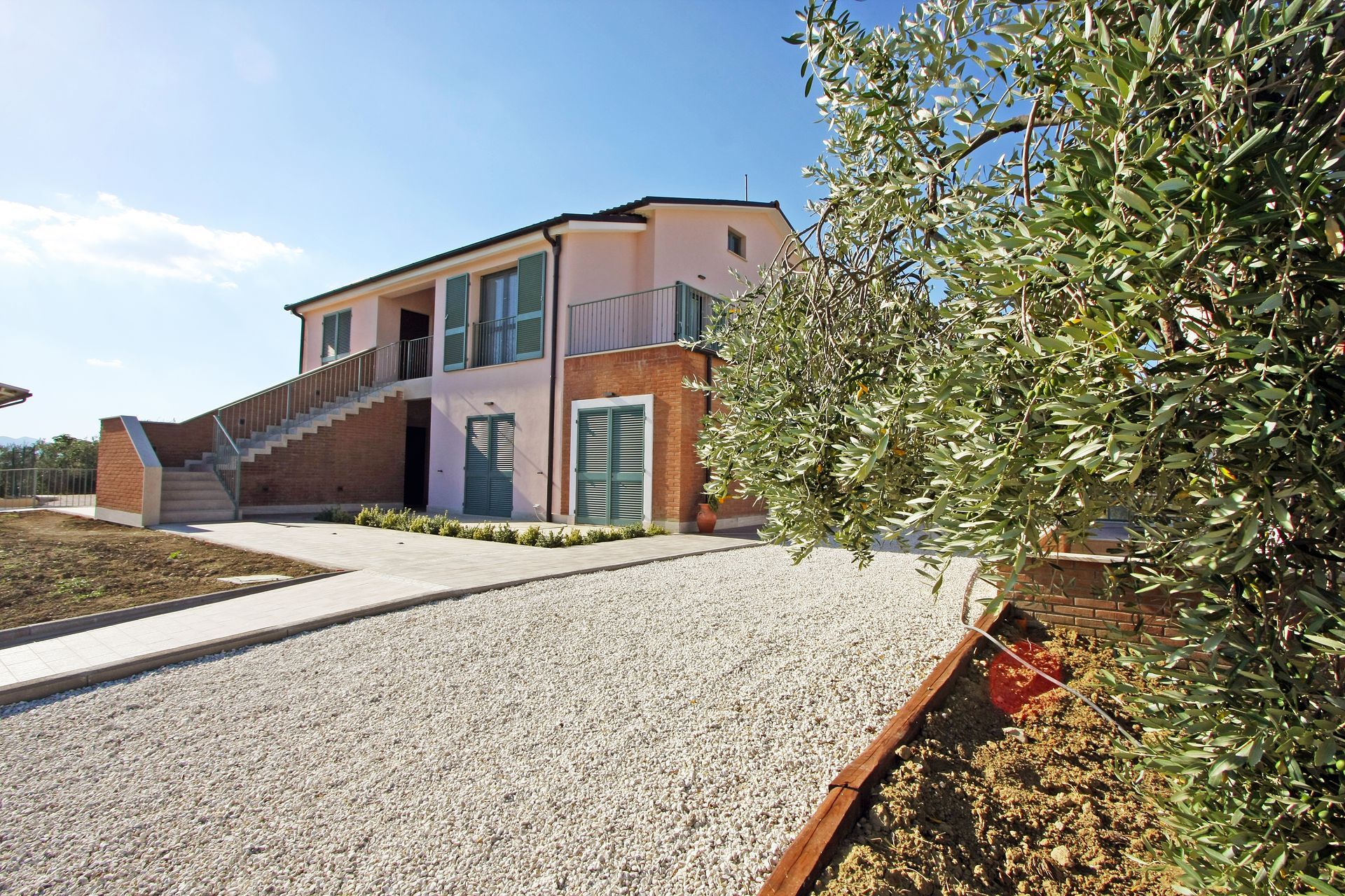 Una villa rosa chiaro con dettagli in mattoni, una scala esterna e persiane