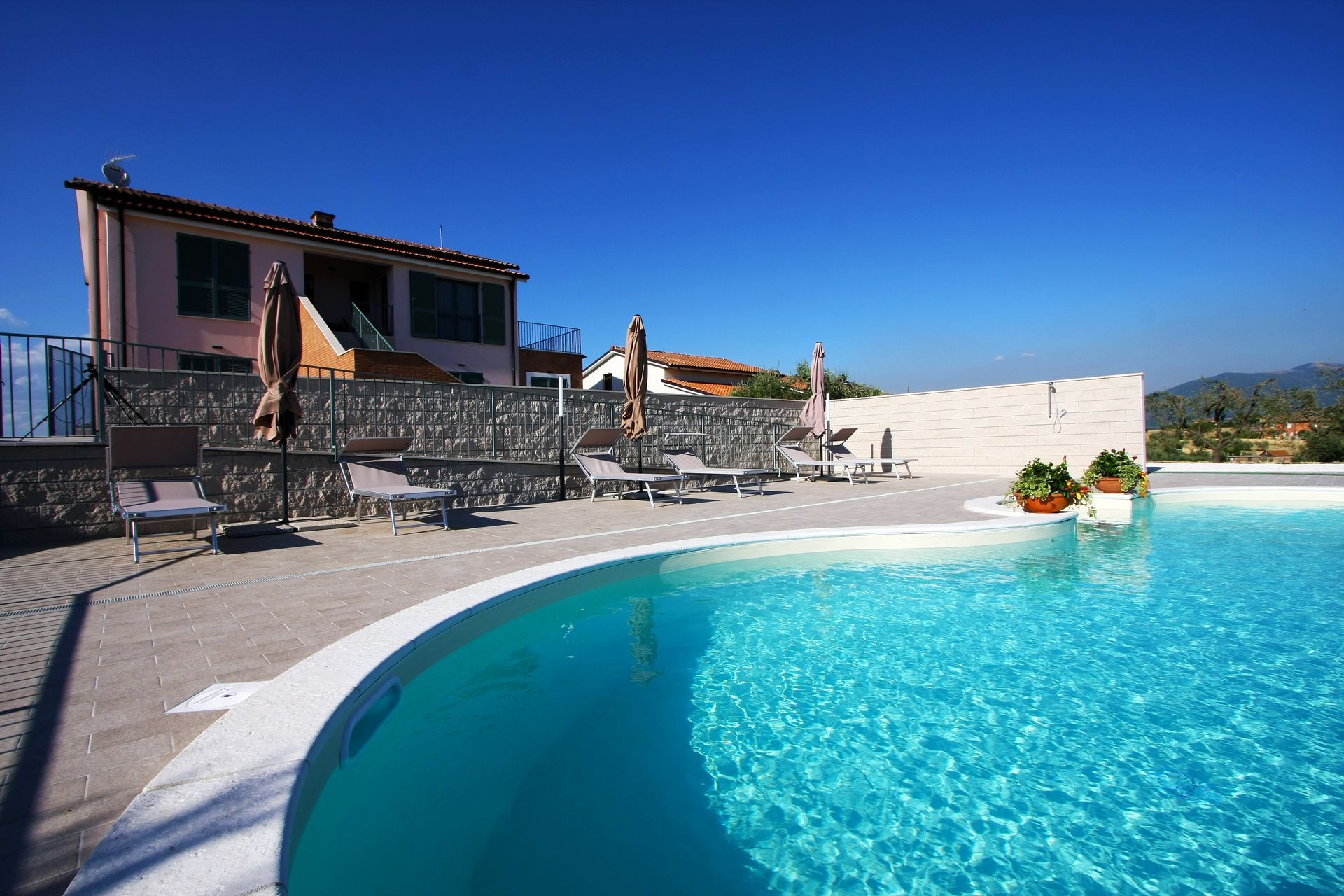 Una piscina turchese su un patio con lettini prendisole, muri in pietra e un