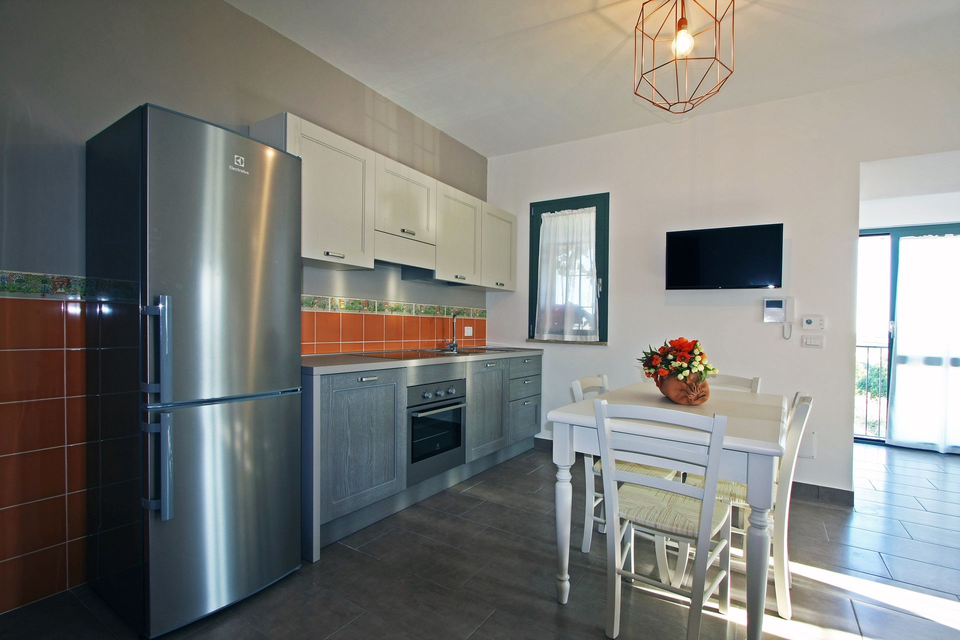 Una cucina con frigorifero in acciaio inox, mobili bianchi, paraschizzi arancione e tavolo da pranzo con sedie.