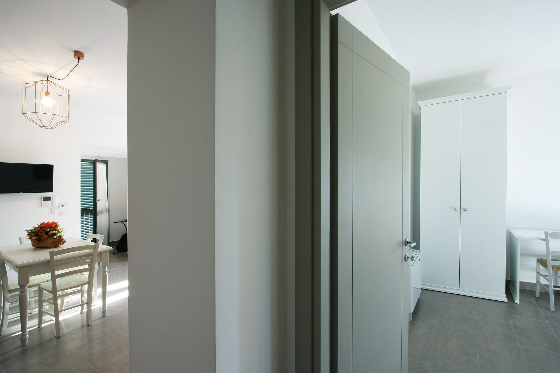 Una vista attraverso una porta su una zona pranzo con tavolo e sedie, adiacente a una stanza con un armadio bianco.
