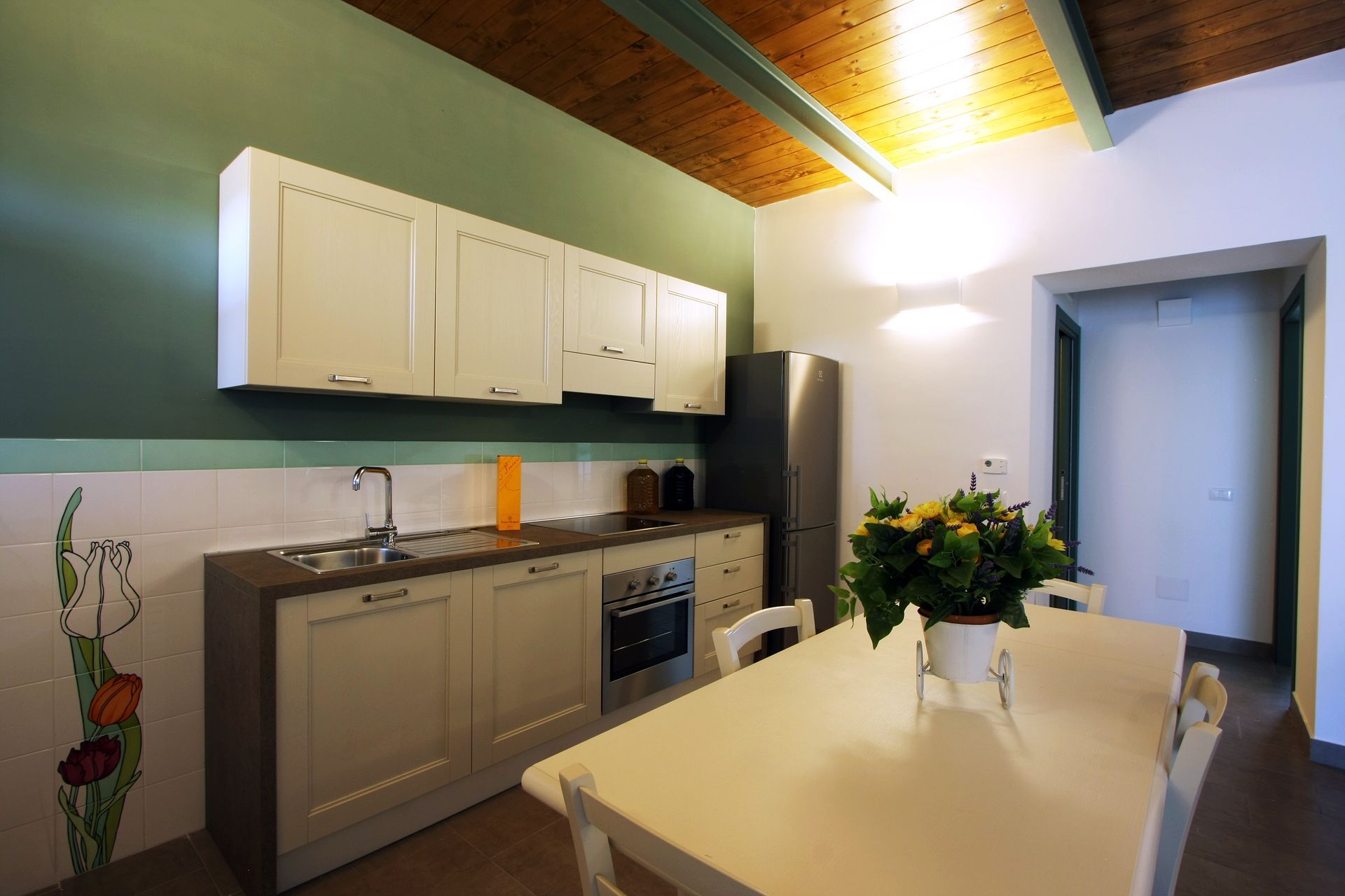 Una cucina moderna con mobili color avorio sporco, ripiani scuri, una parete verde e un tavolo da pranzo con sedie.