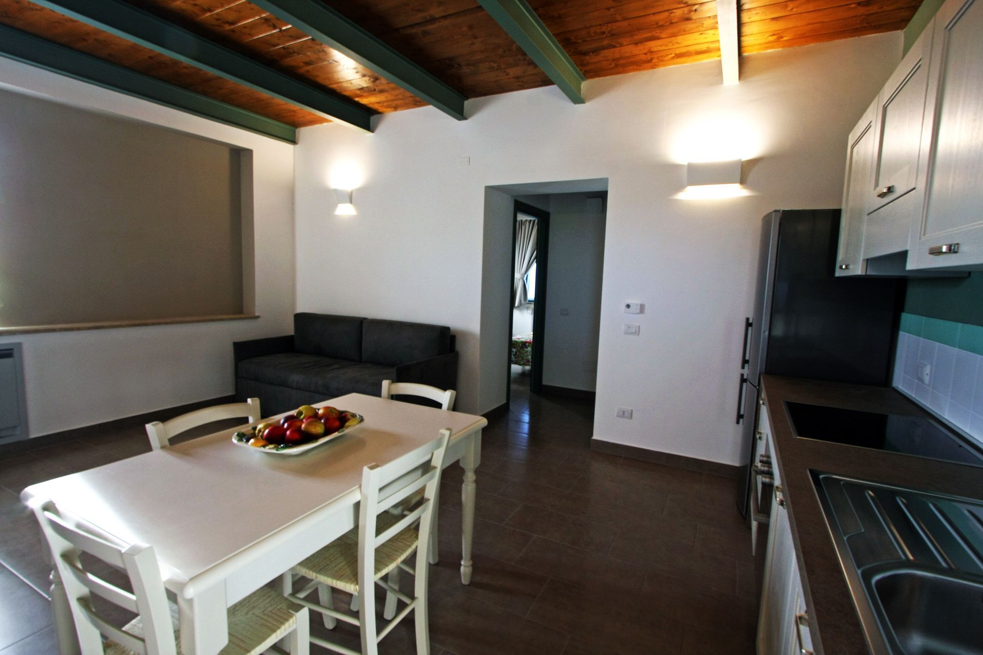 Un appartamento moderno a pianta aperta con un tavolo da pranzo bianco, un divano scuro e una zona cucina con mobili chiari.