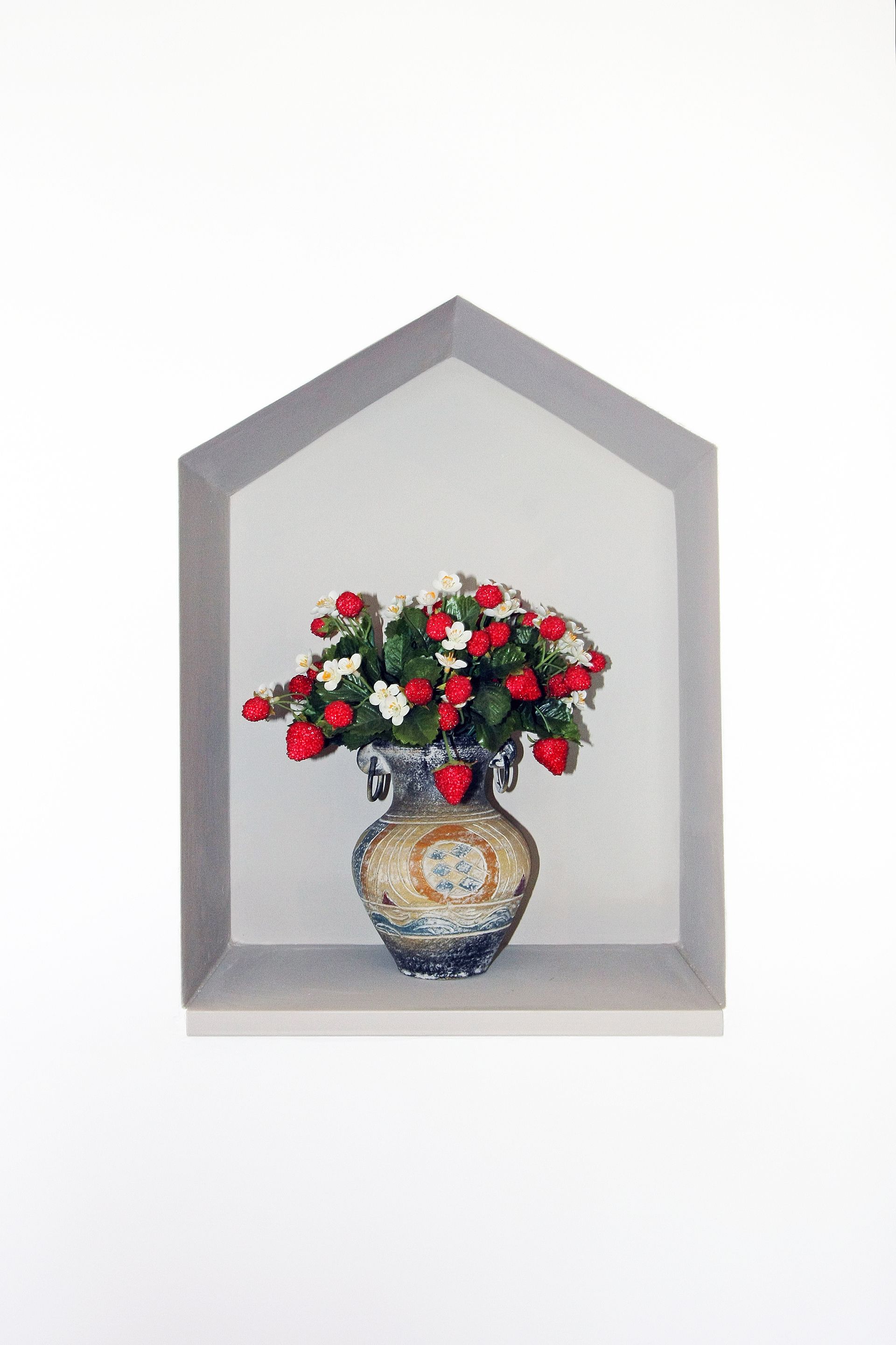 Un vaso di fiori rossi e bianchi è collocato all'interno di una nicchia a muro grigia a forma di casa.