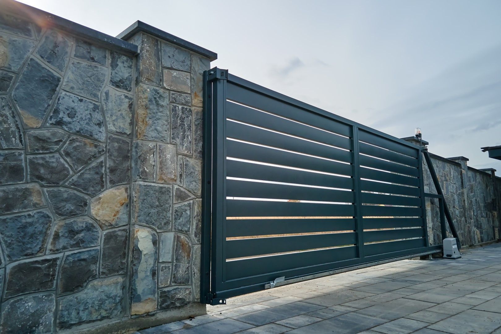 A black sliding gate is sitting in front of a stone wall.