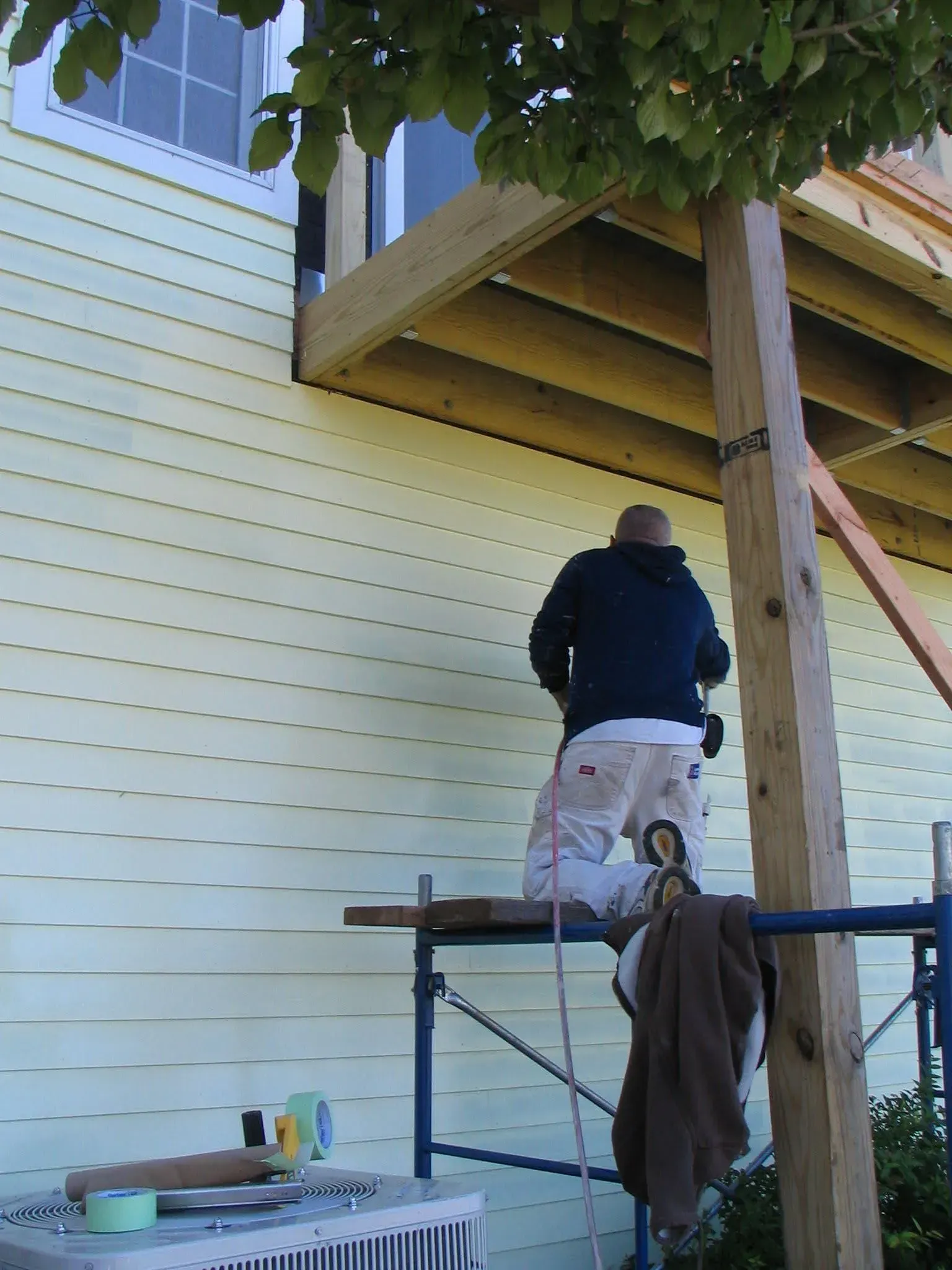 A man is kneeling on a scaffolding in front of a house