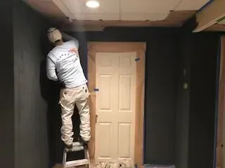 A man is standing on a ladder in a room painting a door.