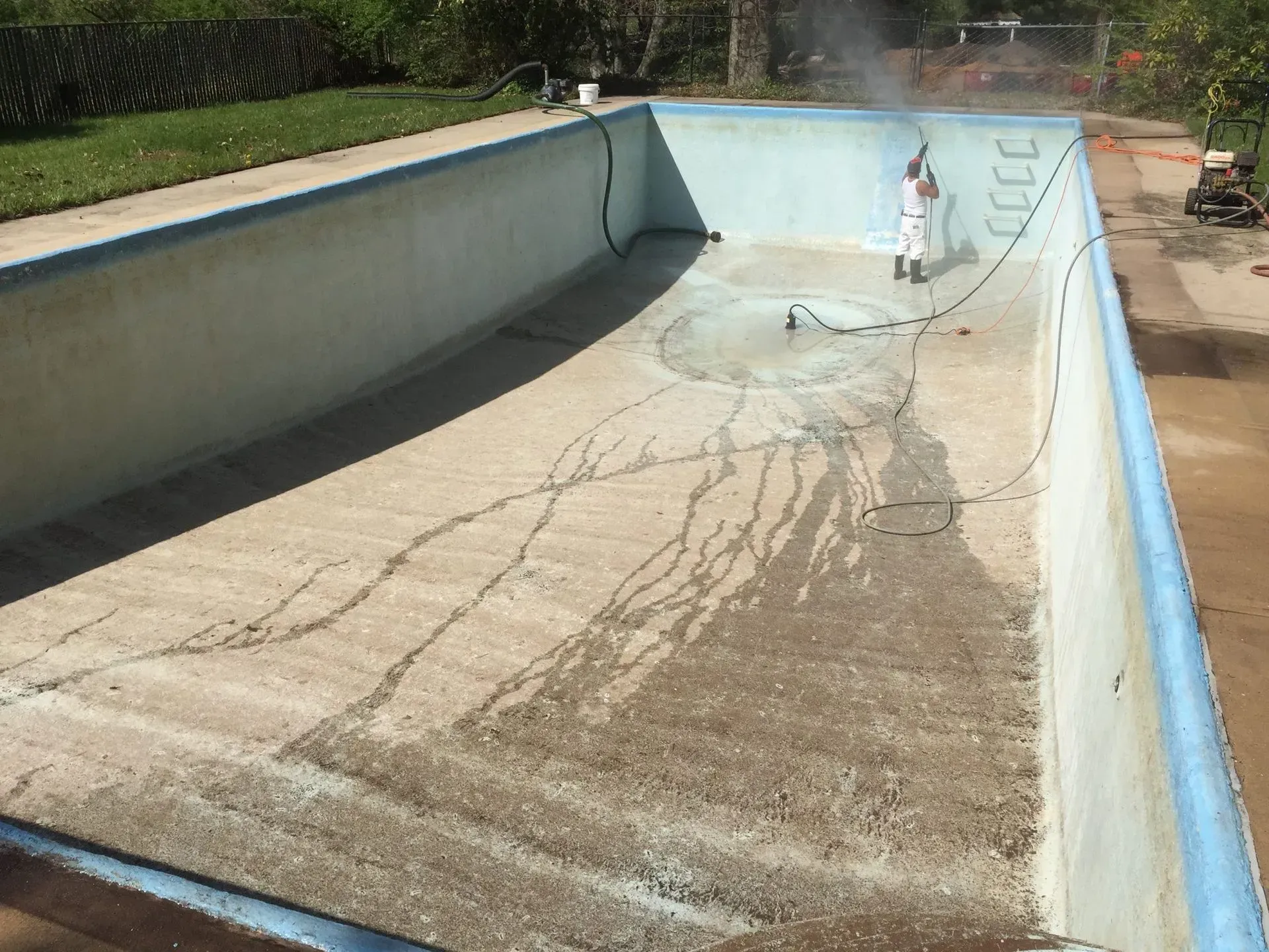 A person is cleaning a swimming pool with a hose