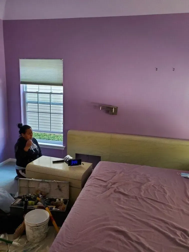 A woman is sitting in a bedroom with purple walls and a bed.