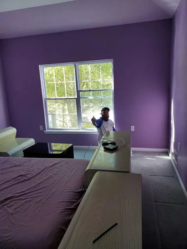 A man is standing in a bedroom with purple walls.