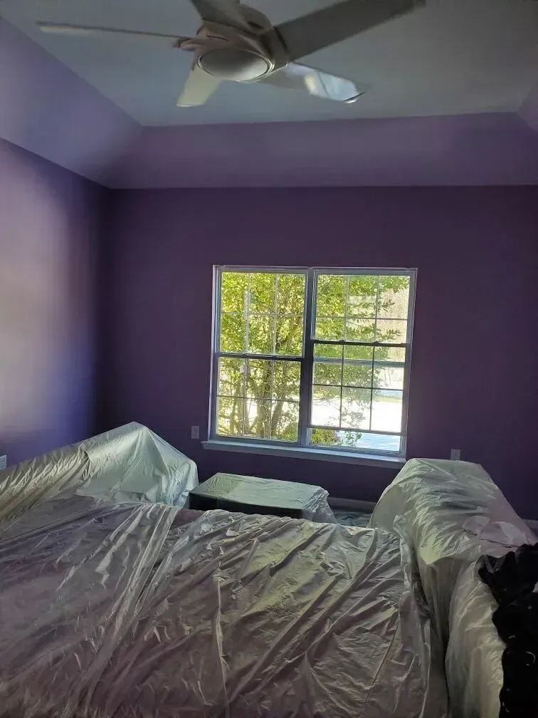 A bedroom with purple walls and a ceiling fan.