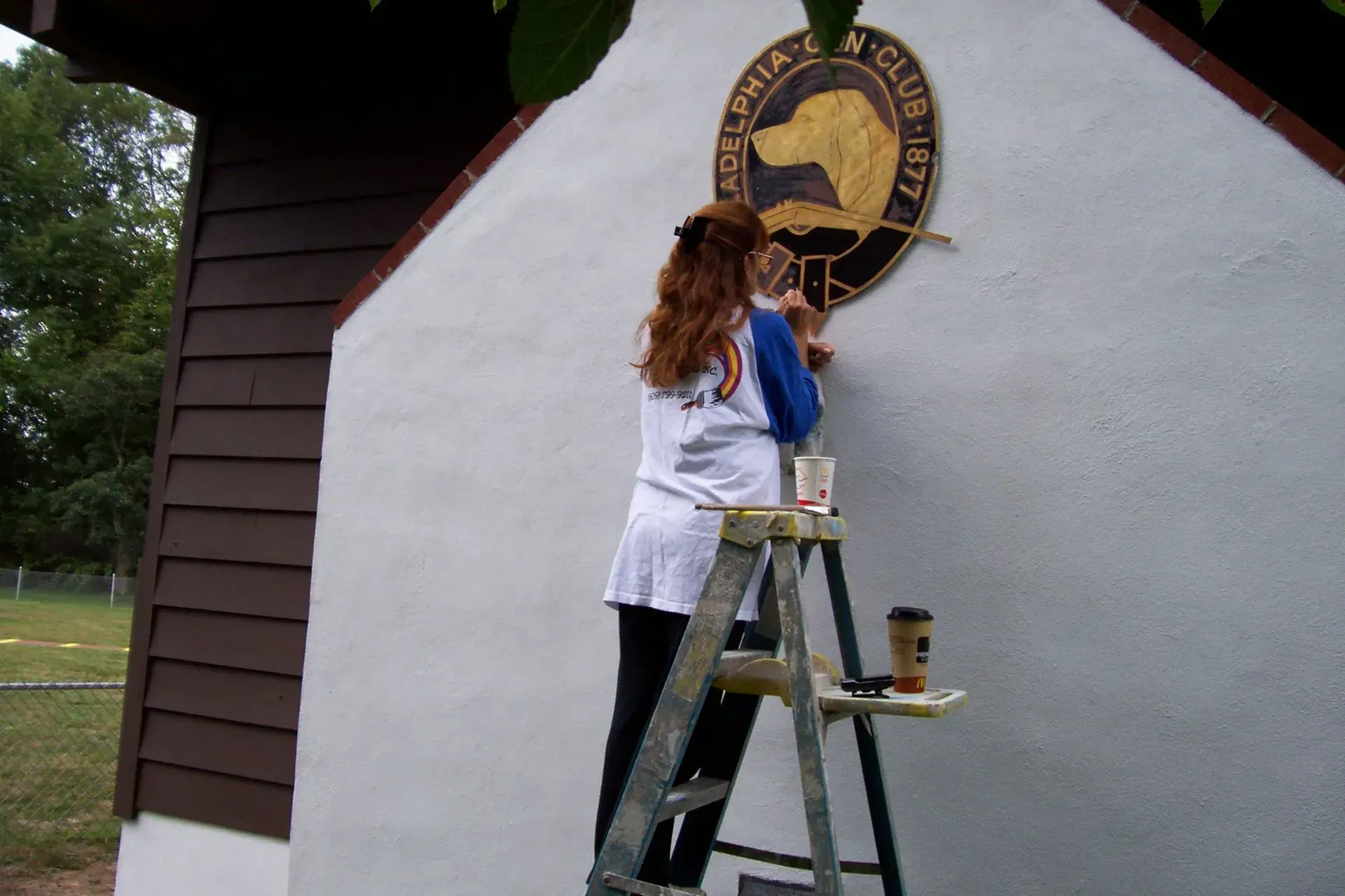 A woman standing on a ladder painting a sign on a wall