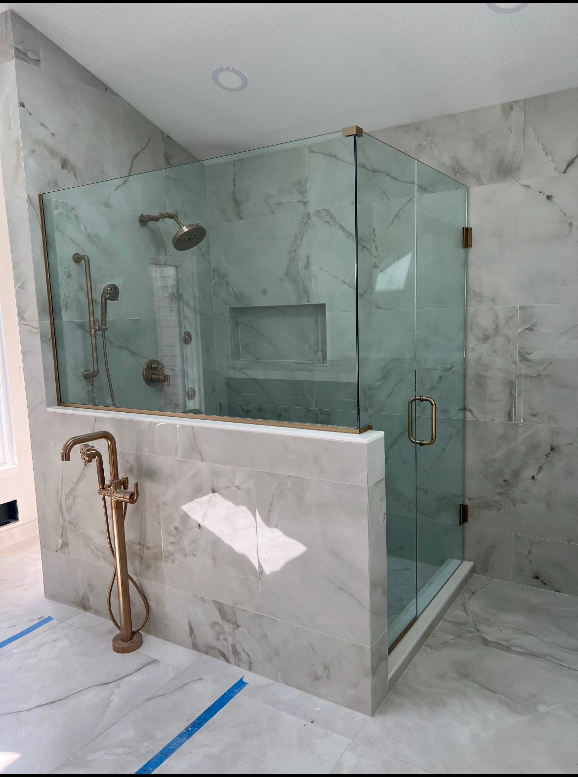 Modern, marble-tiled bathroom with glass shower enclosure, bronze fixtures, and built-in shower niche.