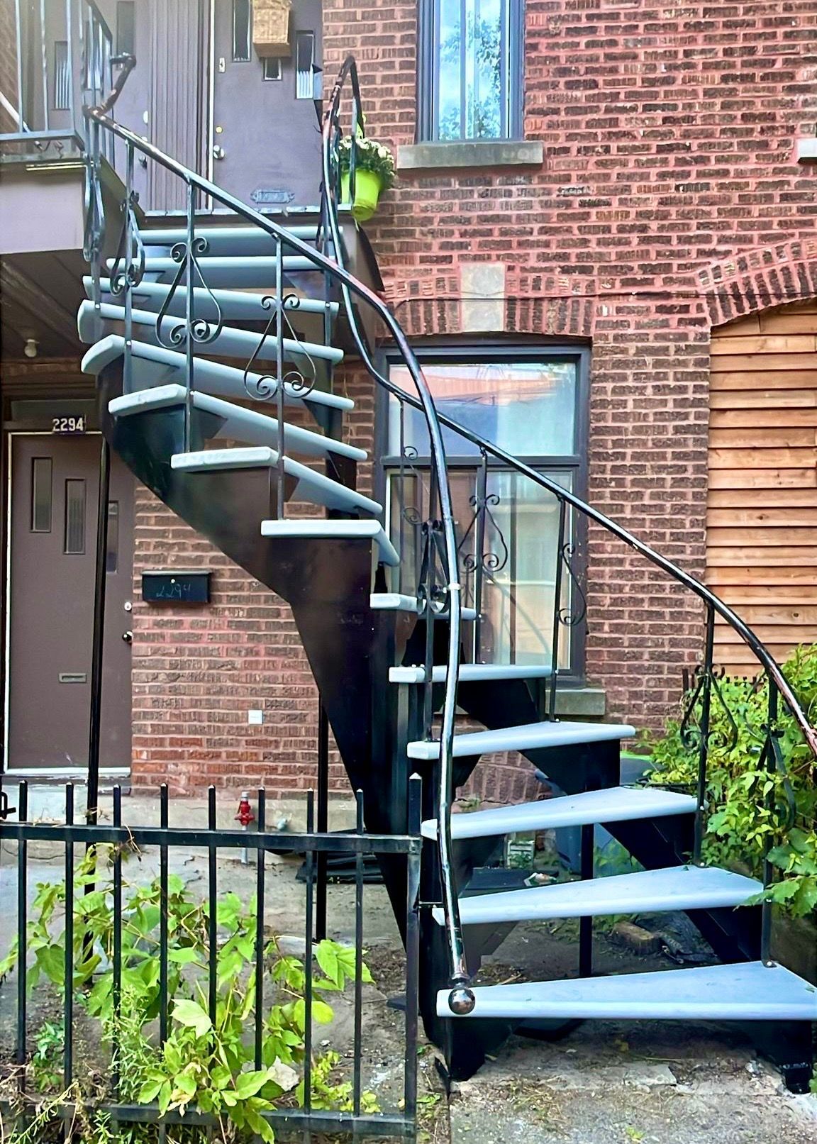 Escalier en colimaçon en métal noir sur un bâtiment en briques rouges.