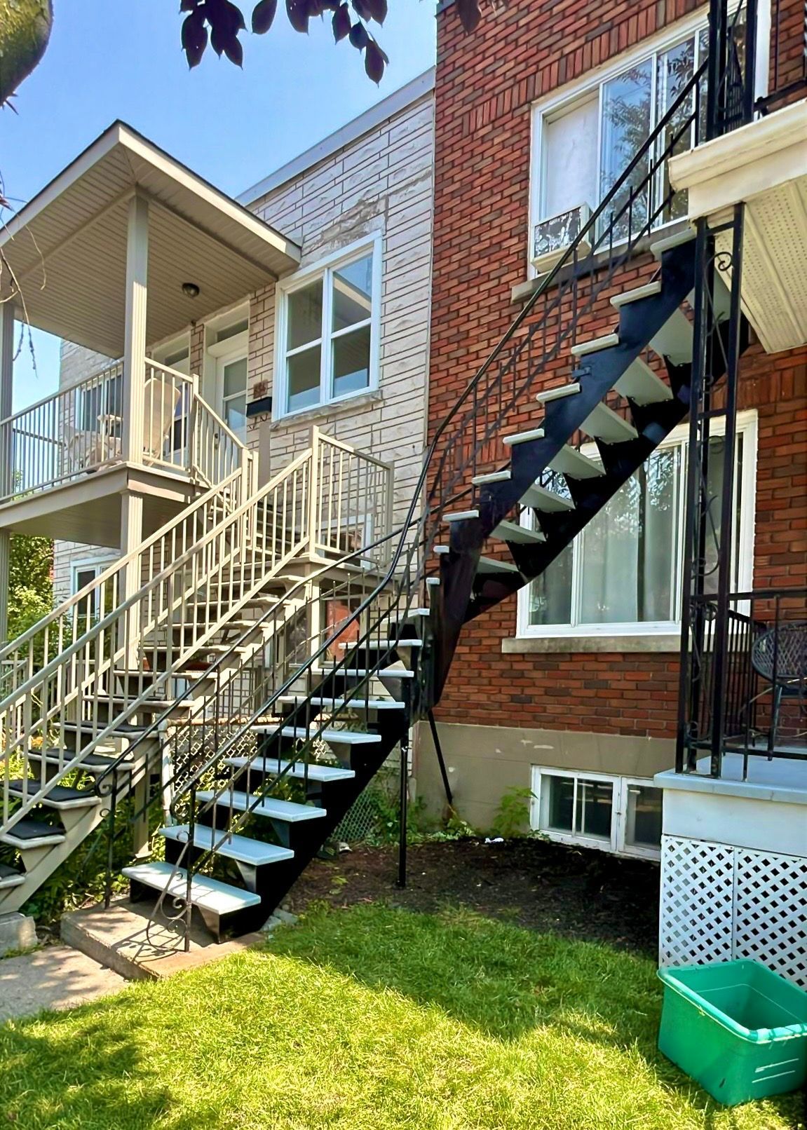 Extérieur d'un bâtiment à deux étages avec escaliers extérieurs ; un en bois, un en métal et une herbe verte luxuriante.