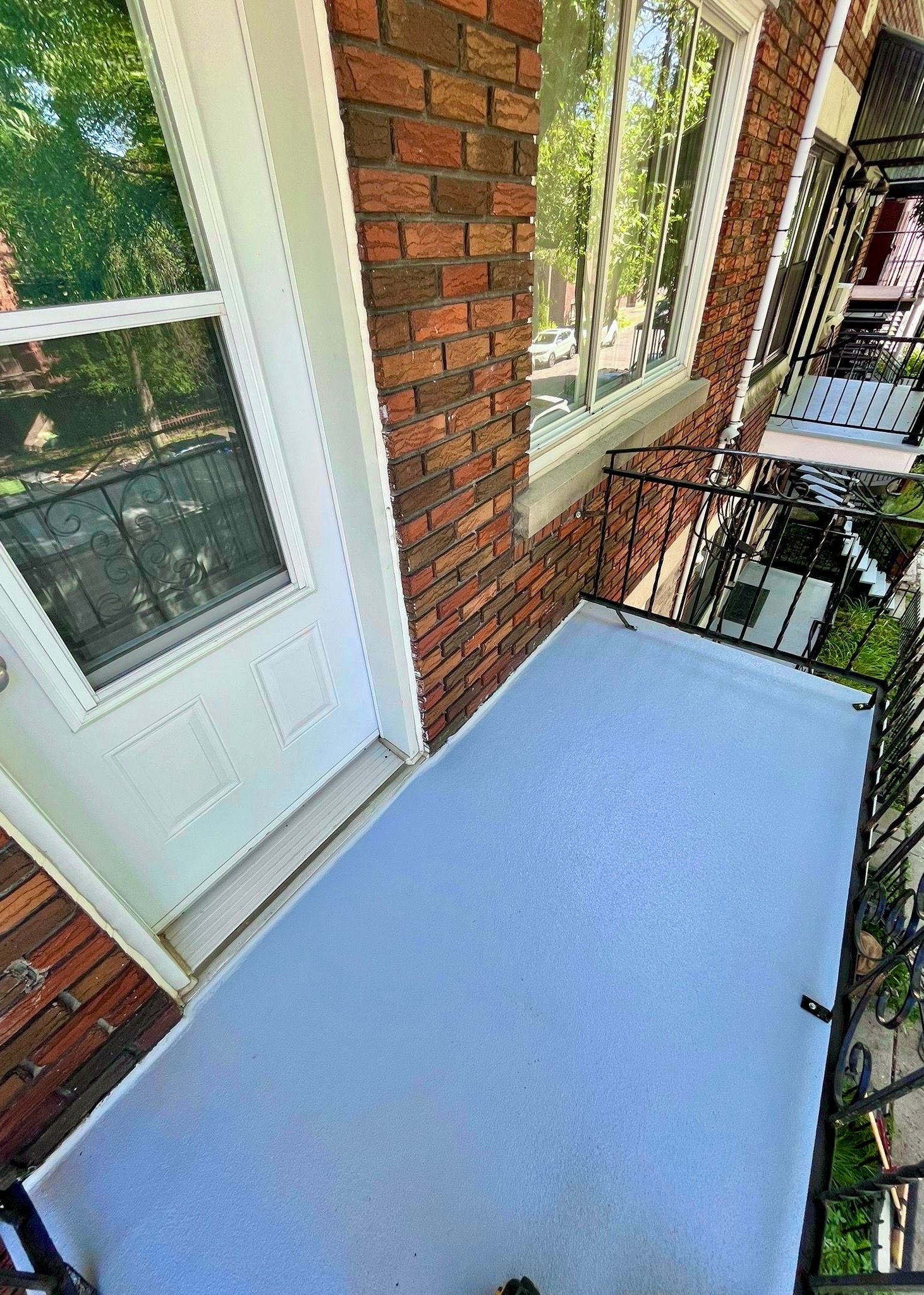 Un petit bâtiment en briques avec une porte et un porche blancs, une rampe et une fenêtre noires.