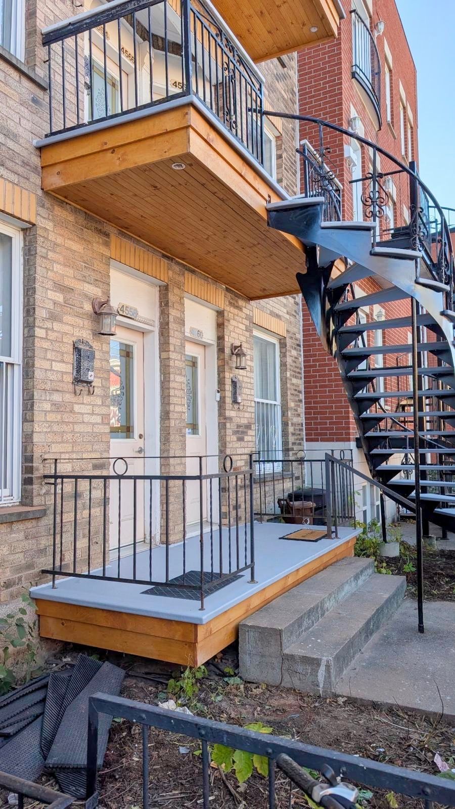 Bâtiment en briques avec un balcon en bois et un escalier en colimaçon. Des marches grises mènent à l'entrée.