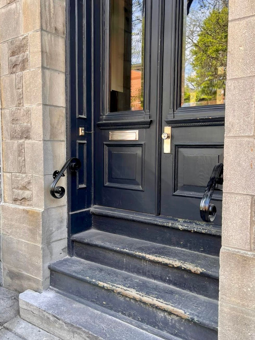 Une porte noire avec des marches menant à elle sur un bâtiment en briques.