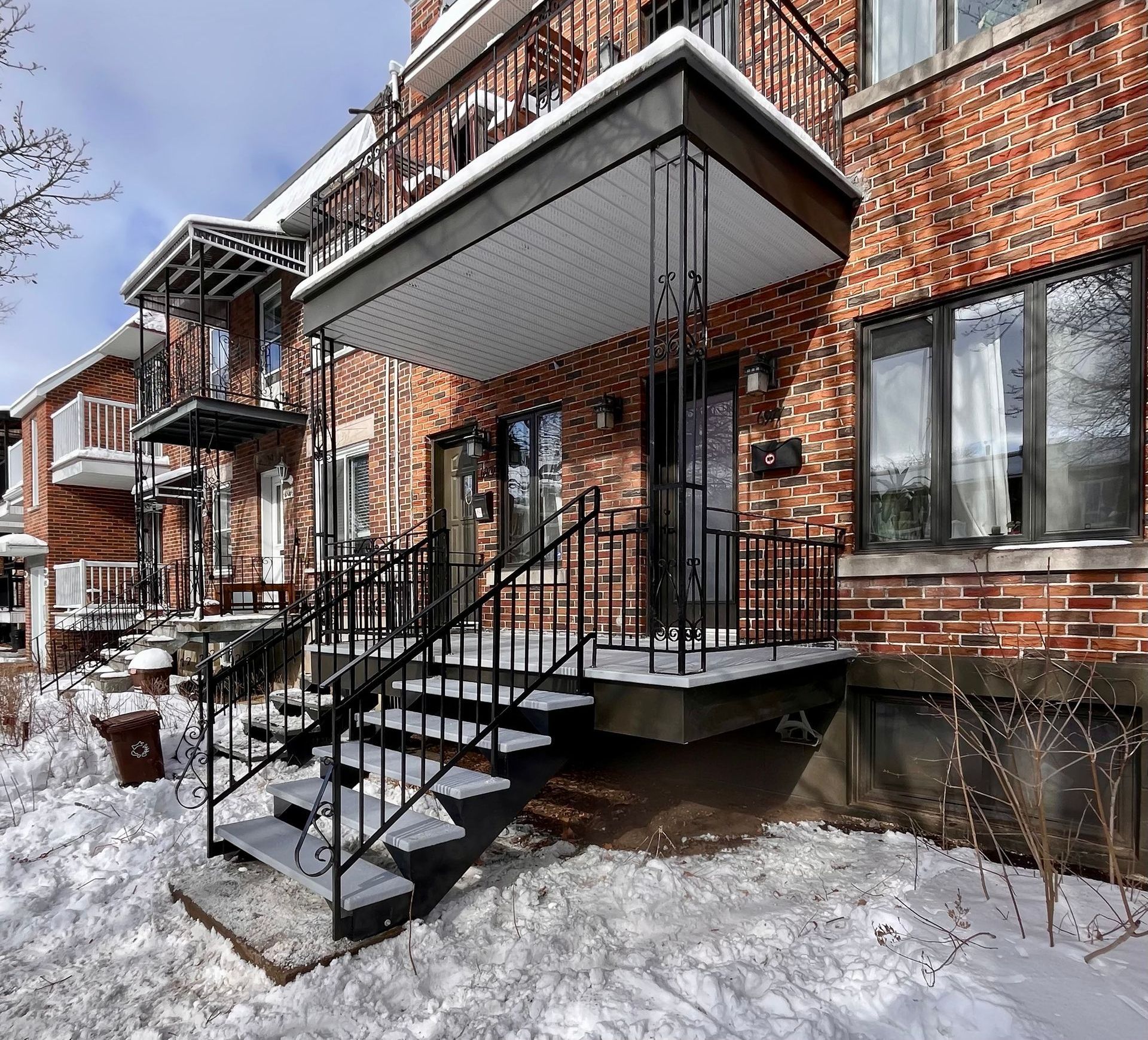Bâtiment en briques avec escaliers en métal noir, rampes et neige au sol.