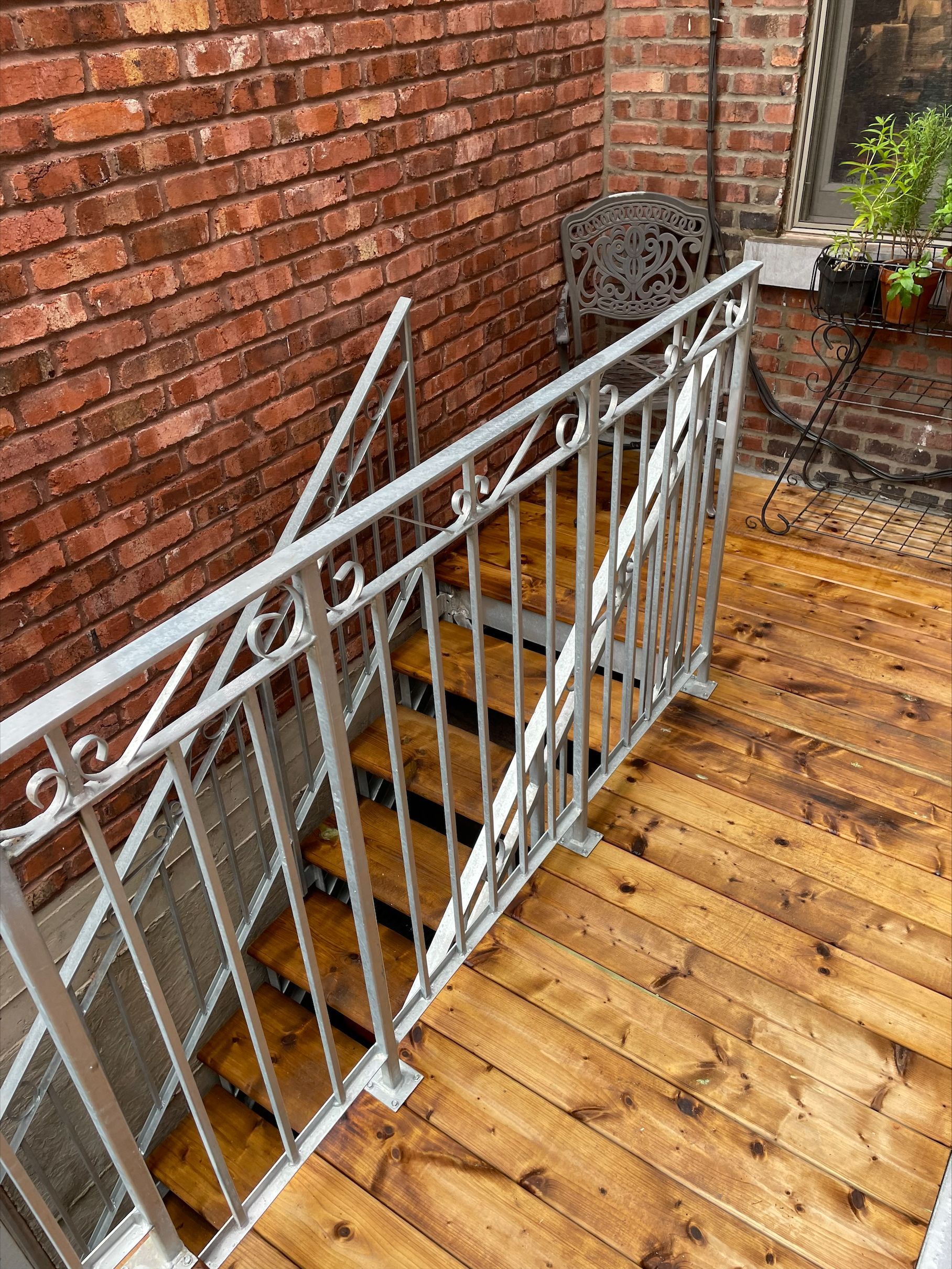 Une terrasse en bois avec des escaliers et une rampe métallique devant un bâtiment en brique.