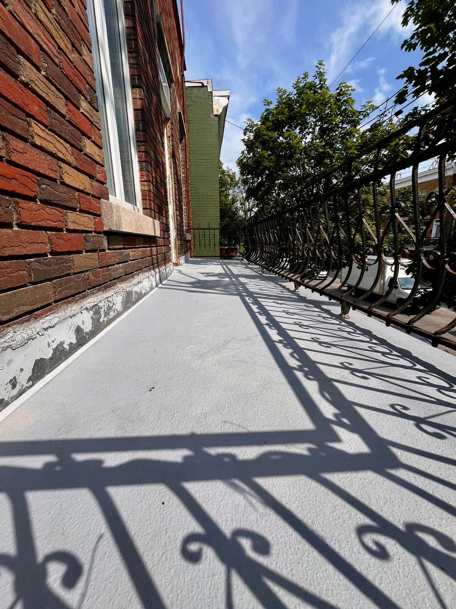 L'ombre d'une balustrade en fer forgé est projetée sur un trottoir à côté d'un bâtiment en briques.