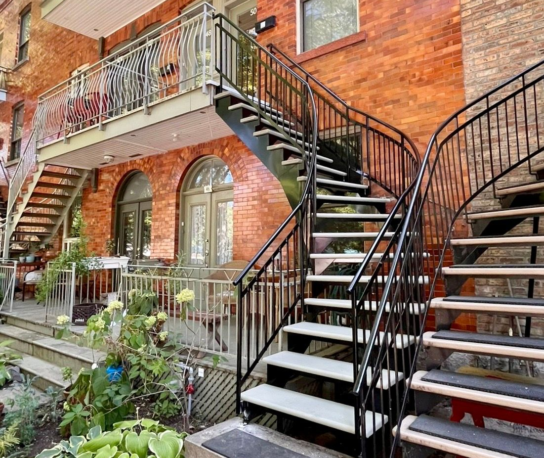 Vue extérieure d'un bâtiment en briques avec plusieurs escaliers et des garde-corps en métal noir.