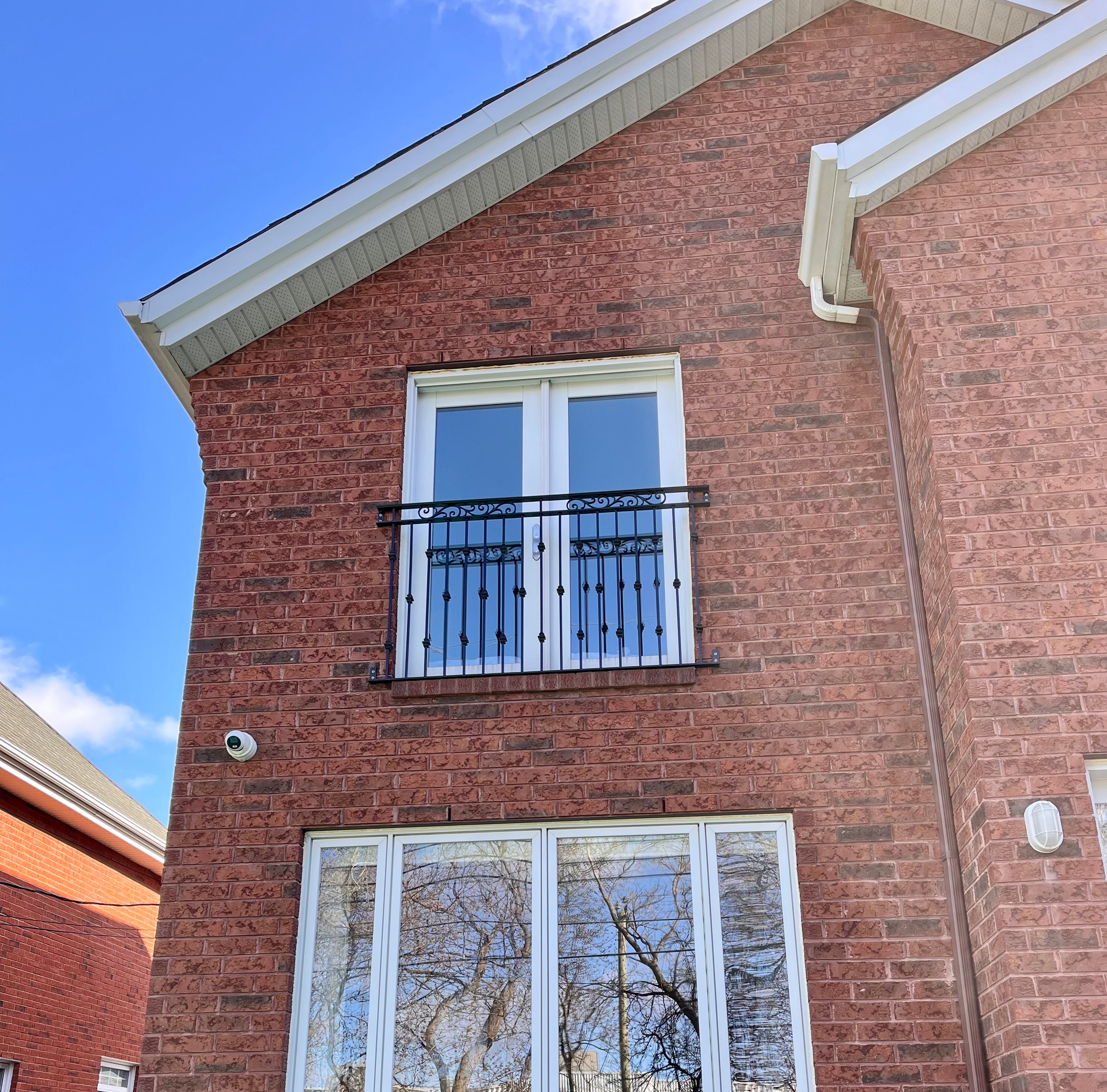 Bâtiment en briques rouges avec fenêtres à bordures blanches. Balcon avec balustrade noire. Ciel bleu.