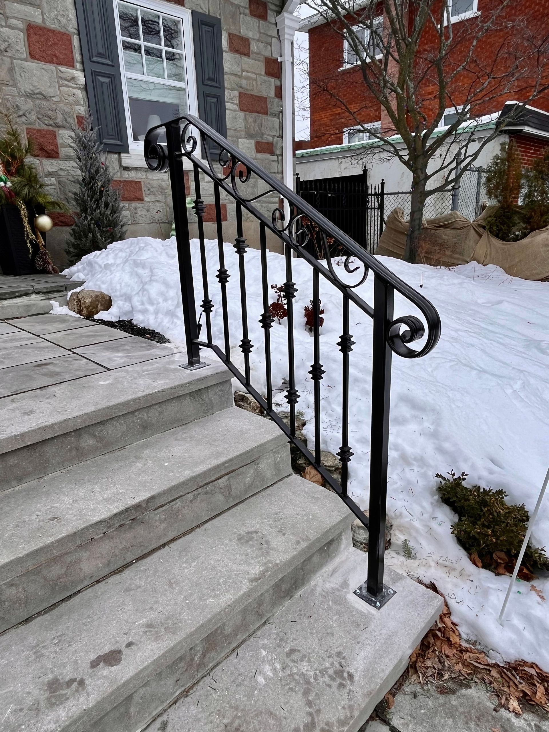 Une balustrade en fer forgé sur un escalier à côté d'une cour enneigée.