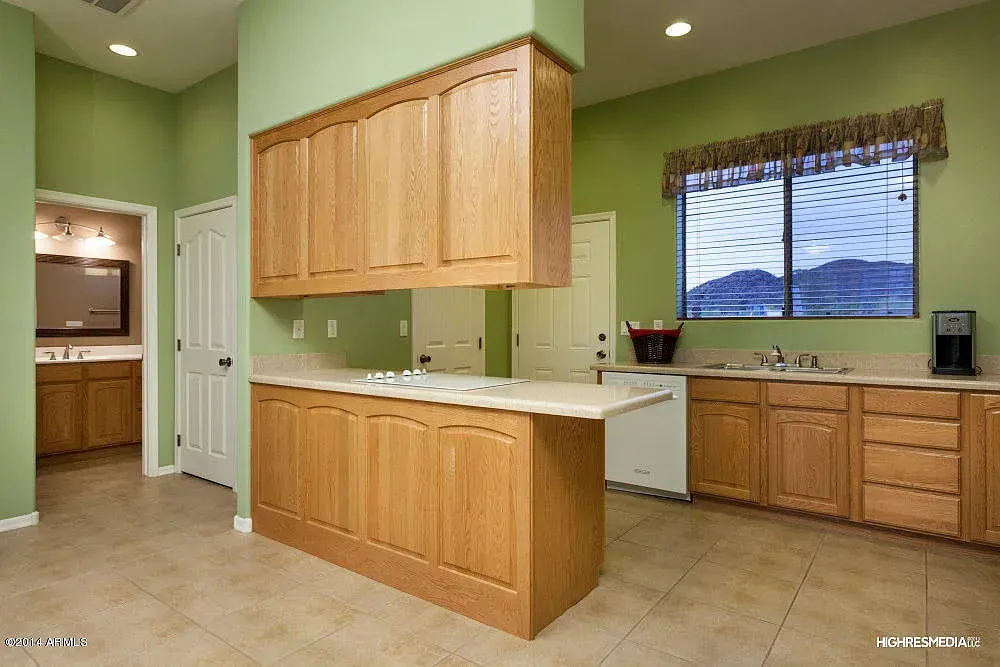 Kitchen with light brown cabinets, sage green walls, and a window with a view.