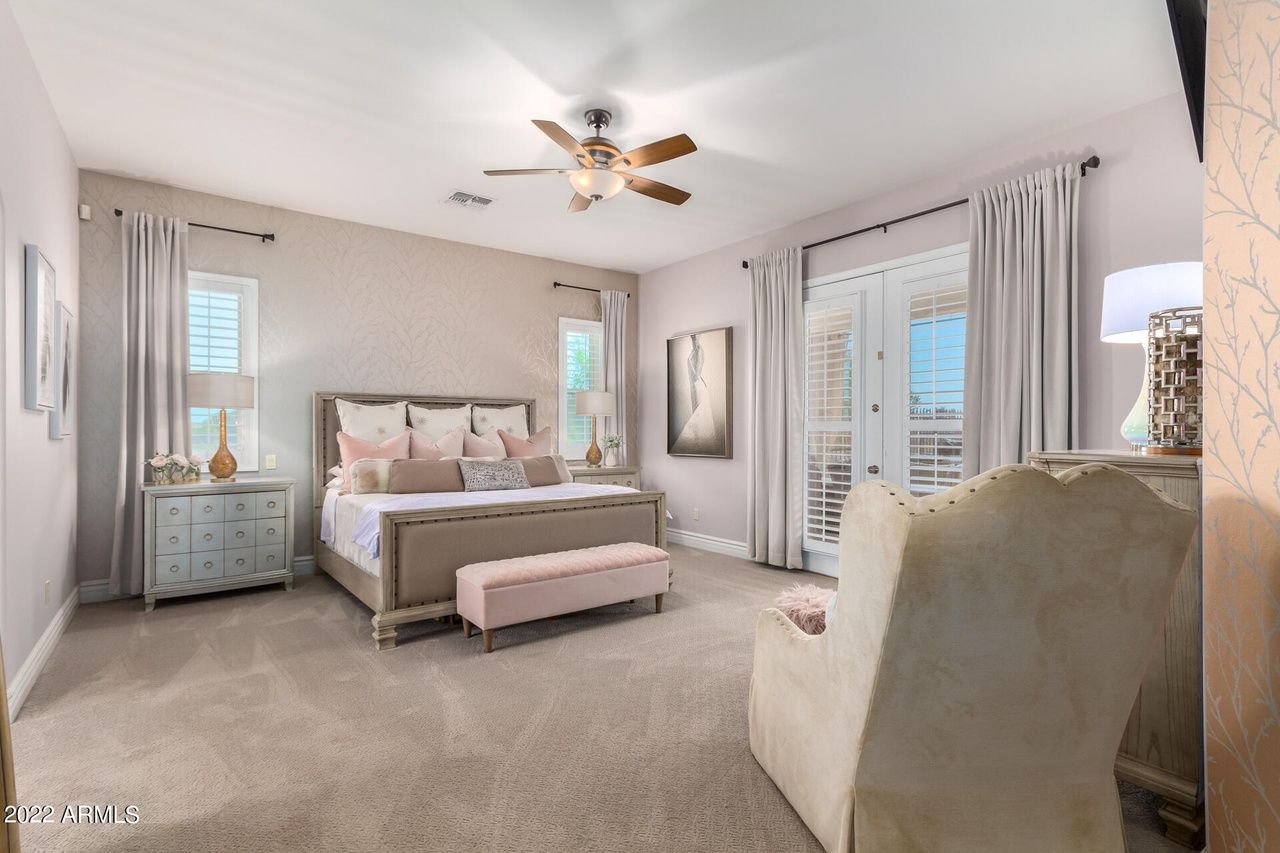 Bedroom with large bed, light pink walls, chair, and balcony doors.