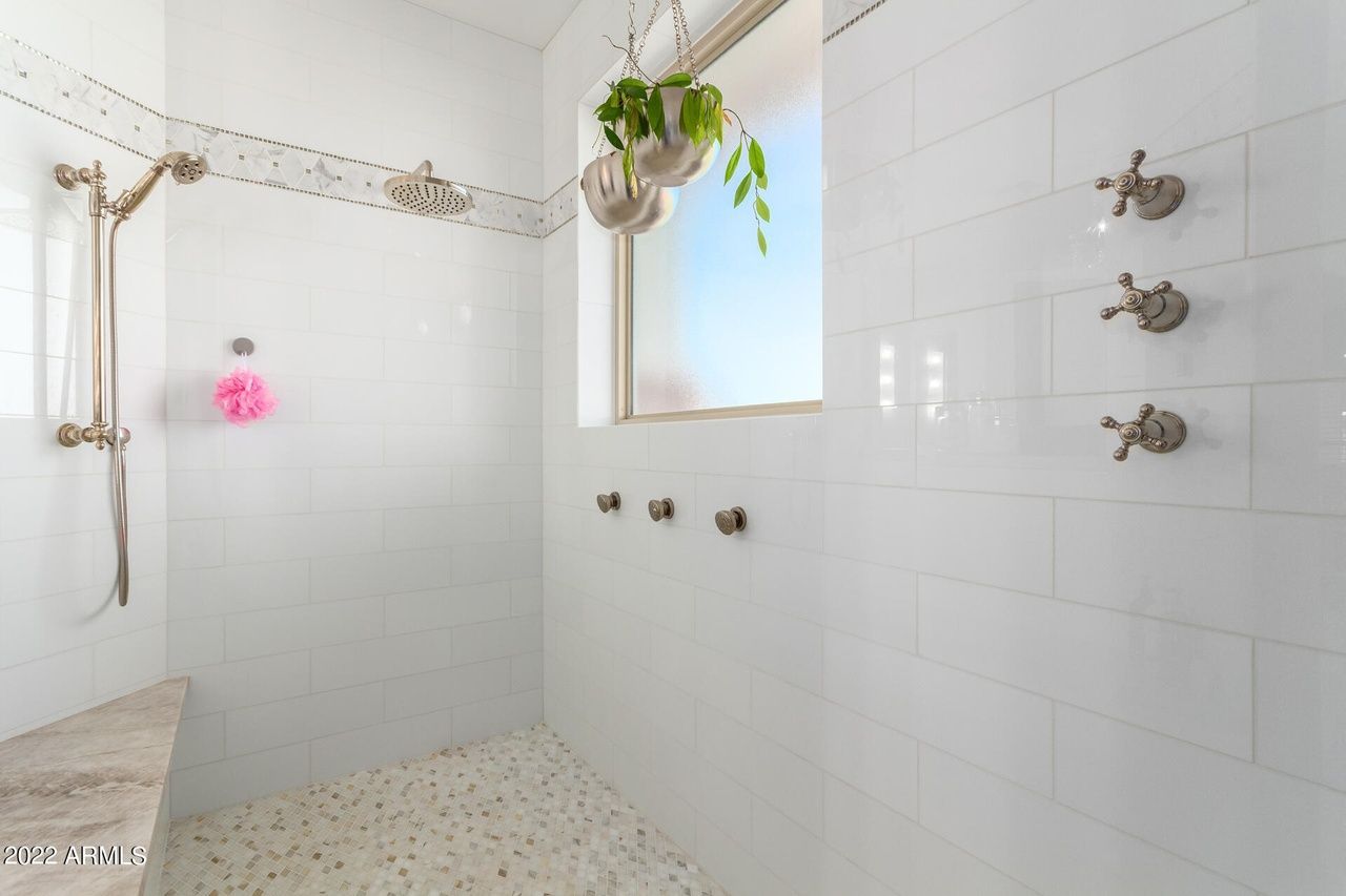 Bright white tiled shower with multiple shower heads, window, and hanging plant.