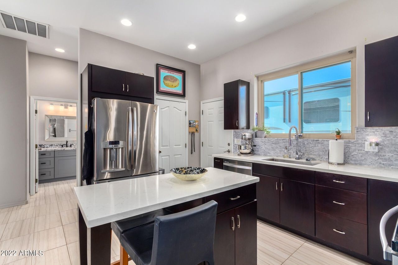 Modern kitchen with dark cabinets, stainless steel fridge, white island, and view of a bathroom.