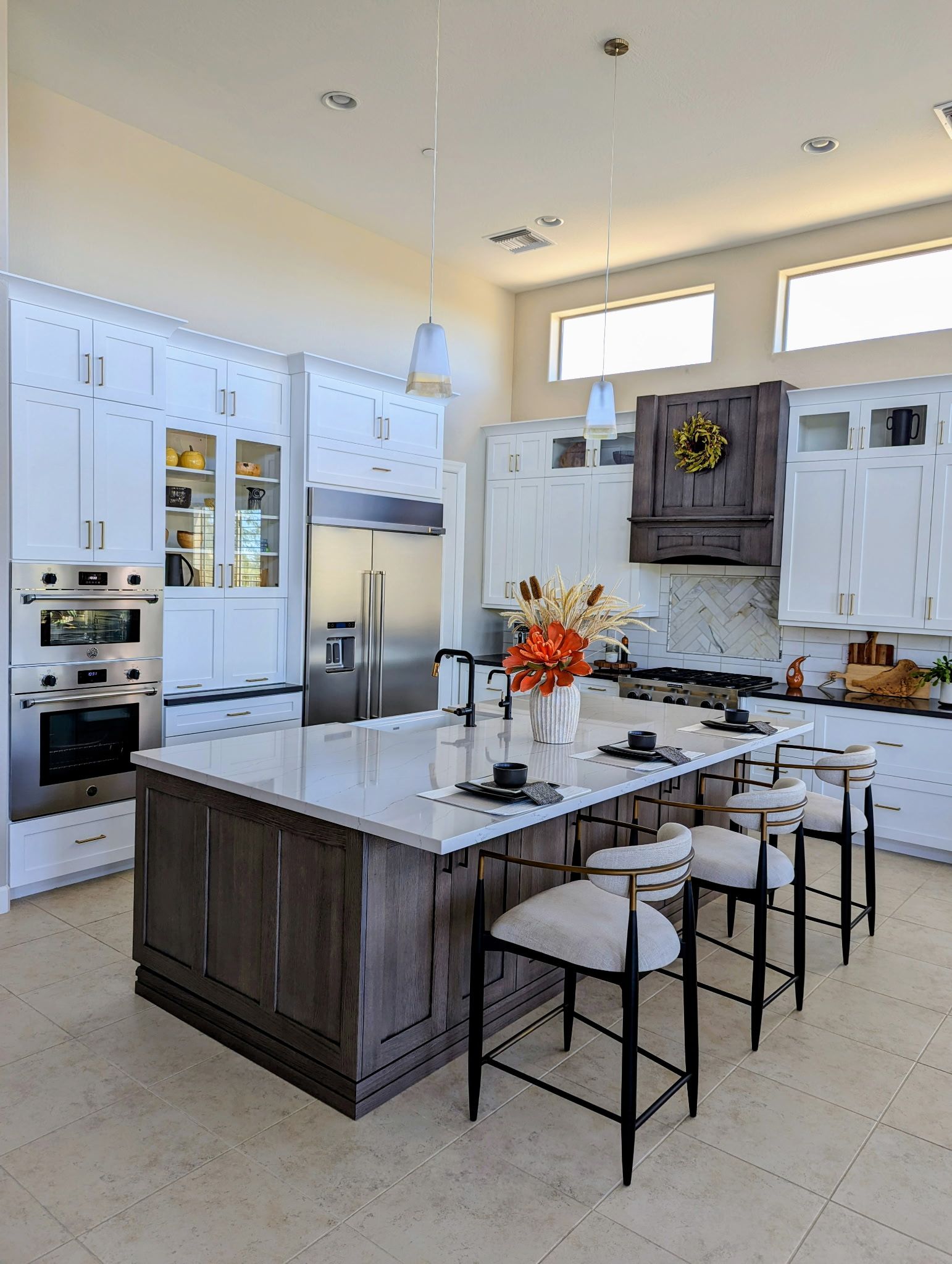 Spacious kitchen with white cabinets, gray island, and stainless steel appliances. High ceilings and neutral colors.