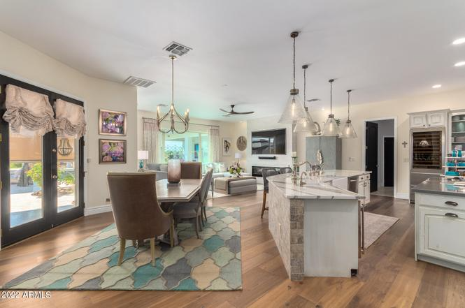 Open-concept dining room, kitchen, and living area; turquoise rug, light fixtures, neutral color palette.