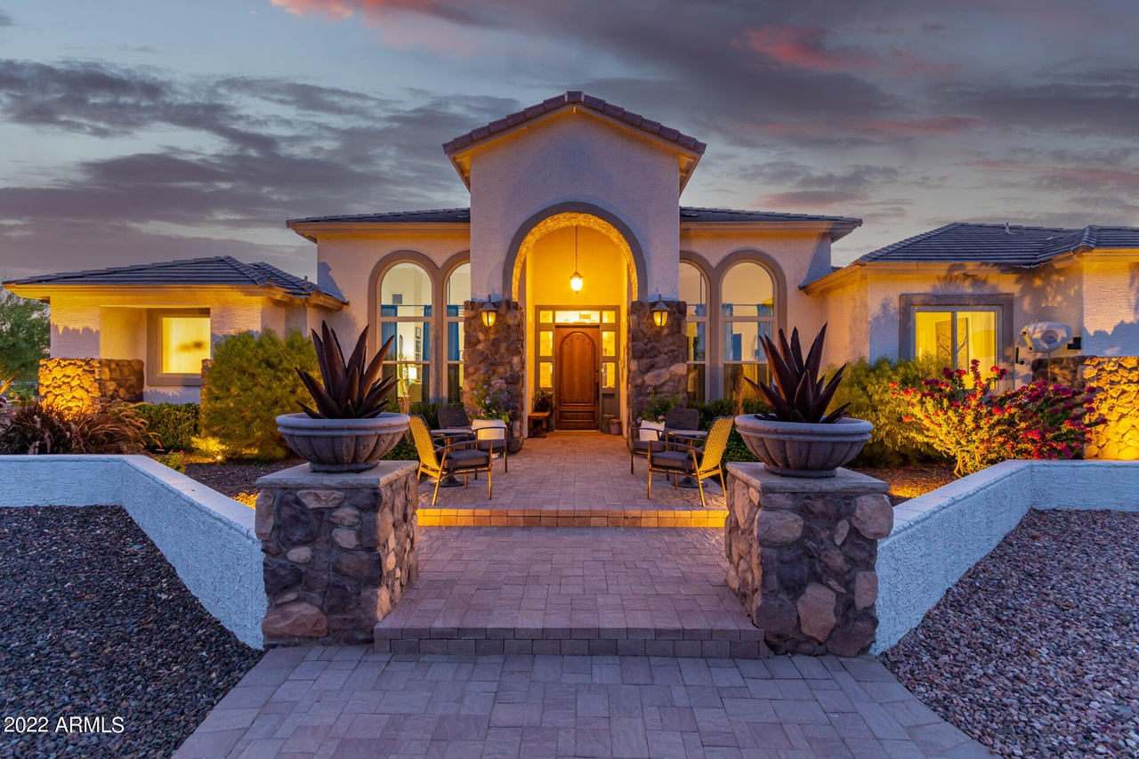 Luxurious home exterior at dusk; stone columns, arched entry, glowing lights.