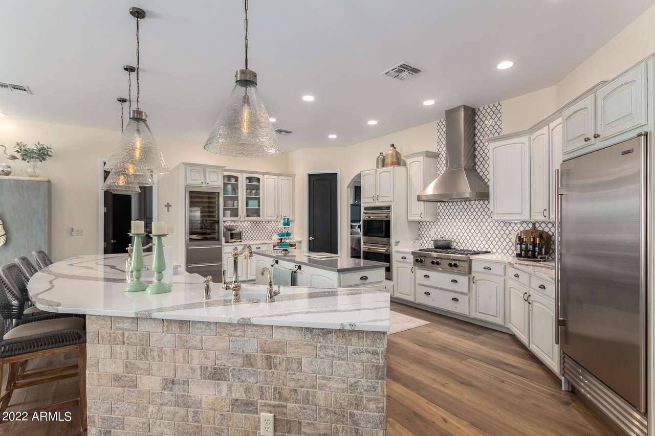 Elegant white kitchen with curved island, stainless steel appliances, and hanging lights.