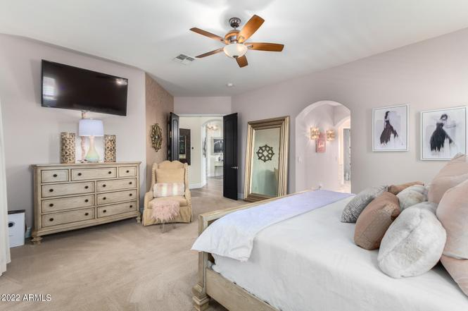 Bedroom with TV, bed, dresser, mirror, and chair; neutral colors.