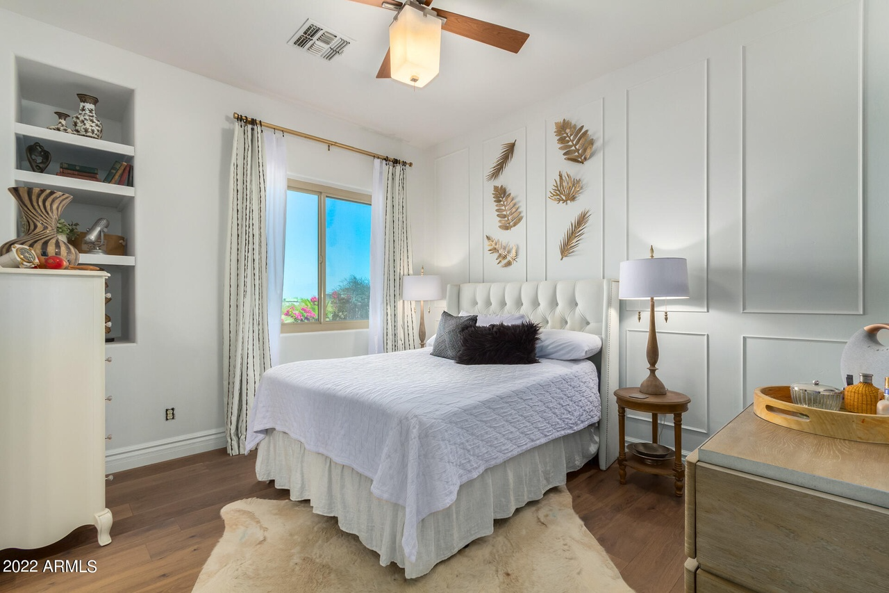 Bedroom with white walls, bed, built-in shelves, and brown hardwood floors.