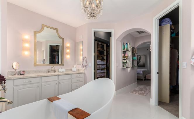 A luxurious pink bathroom with a tub, vanity, walk-in closet, and chandelier.