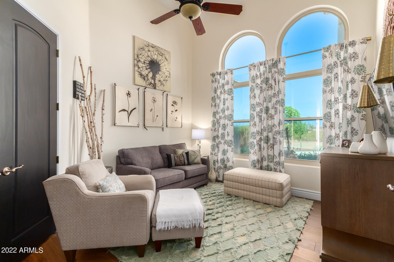 Living room with sofa, armchair, ottoman, floral curtains, and arched windows.