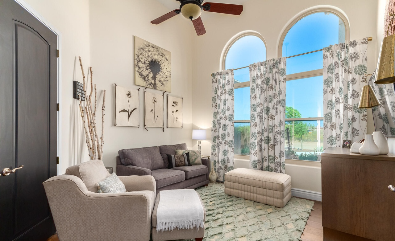 Living room with arched windows, gray sofa, floral curtains, and beige armchair.