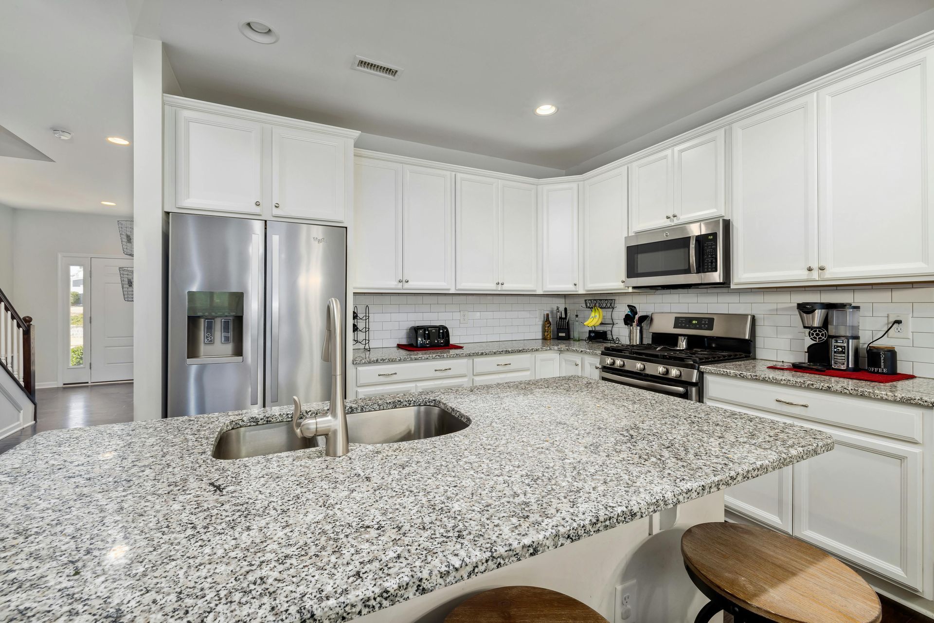 Bright white kitchen with granite countertops and stainless steel appliances.