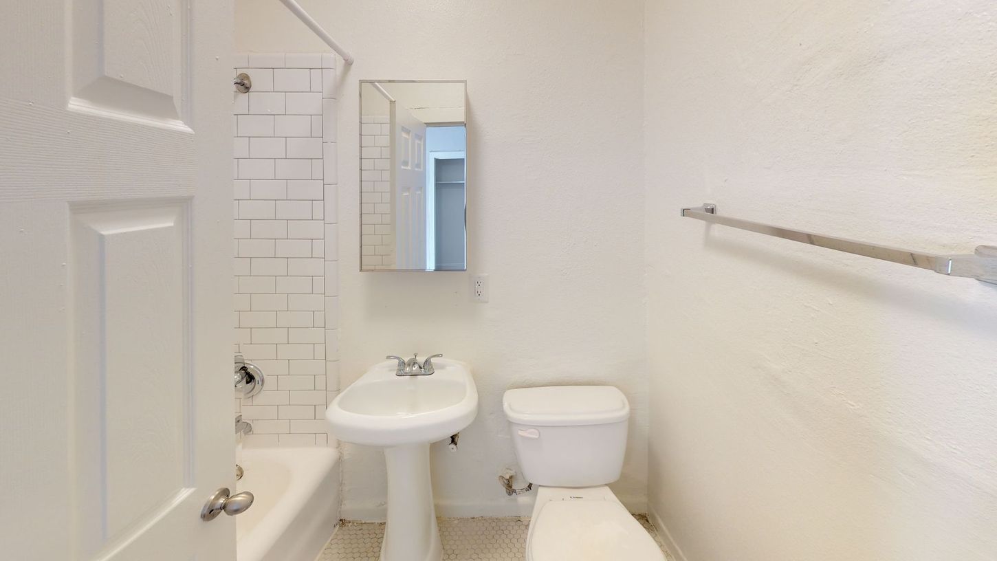 Small bathroom with white walls, pedestal sink, toilet, and a shower/tub.