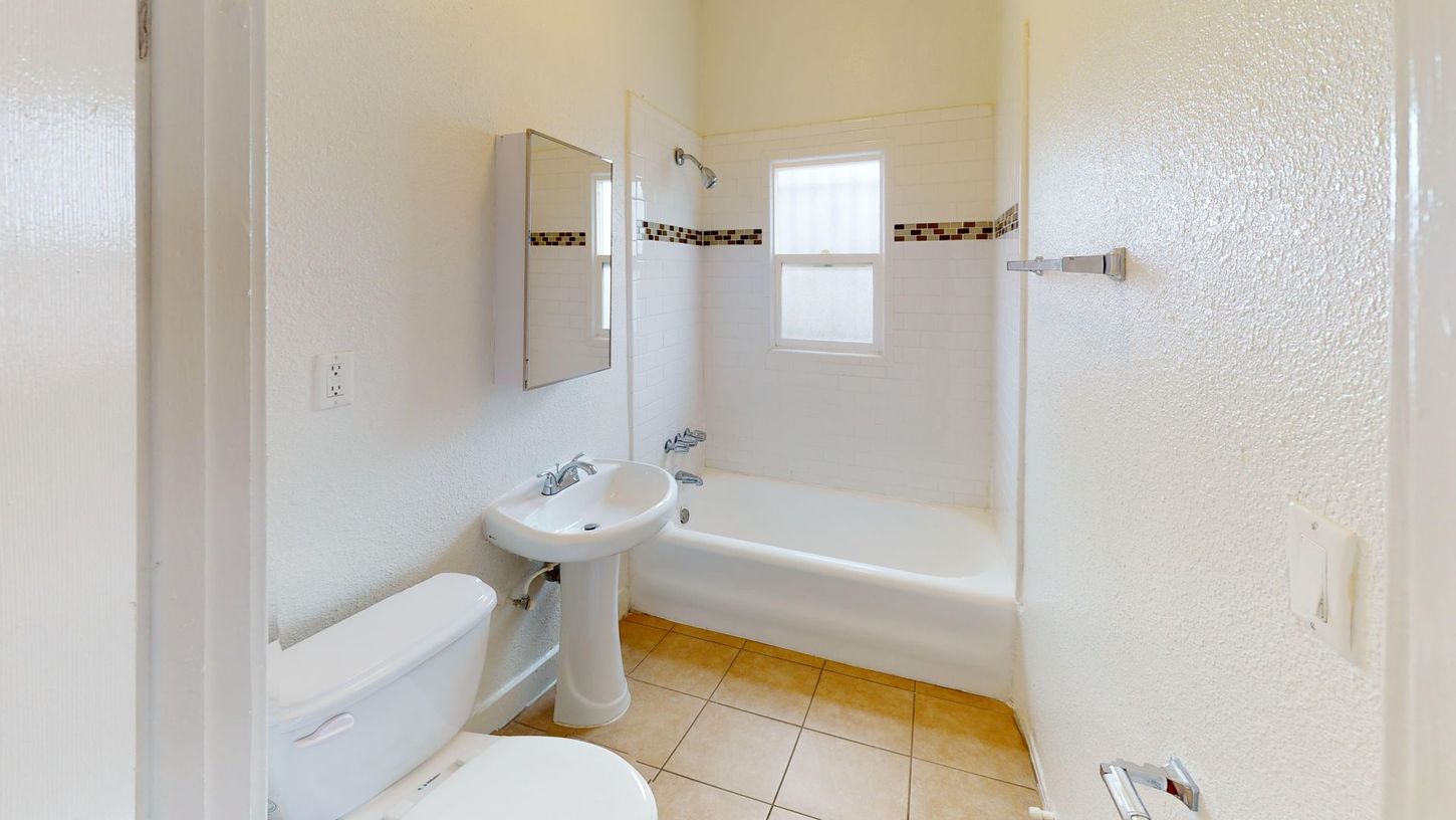 Bathroom with white fixtures, a small window, and tiled floor.