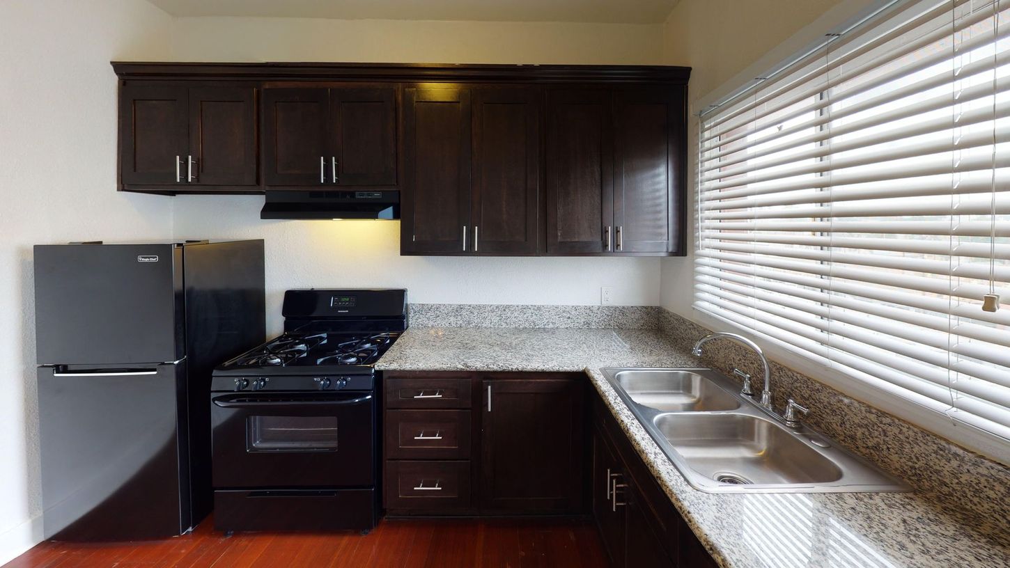 Dark-brown kitchen cabinets and appliances with a granite countertop, sink, and window blinds.