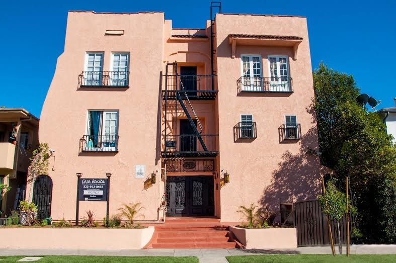 A peach-colored apartment building with a black fire escape, under a blue sky.
