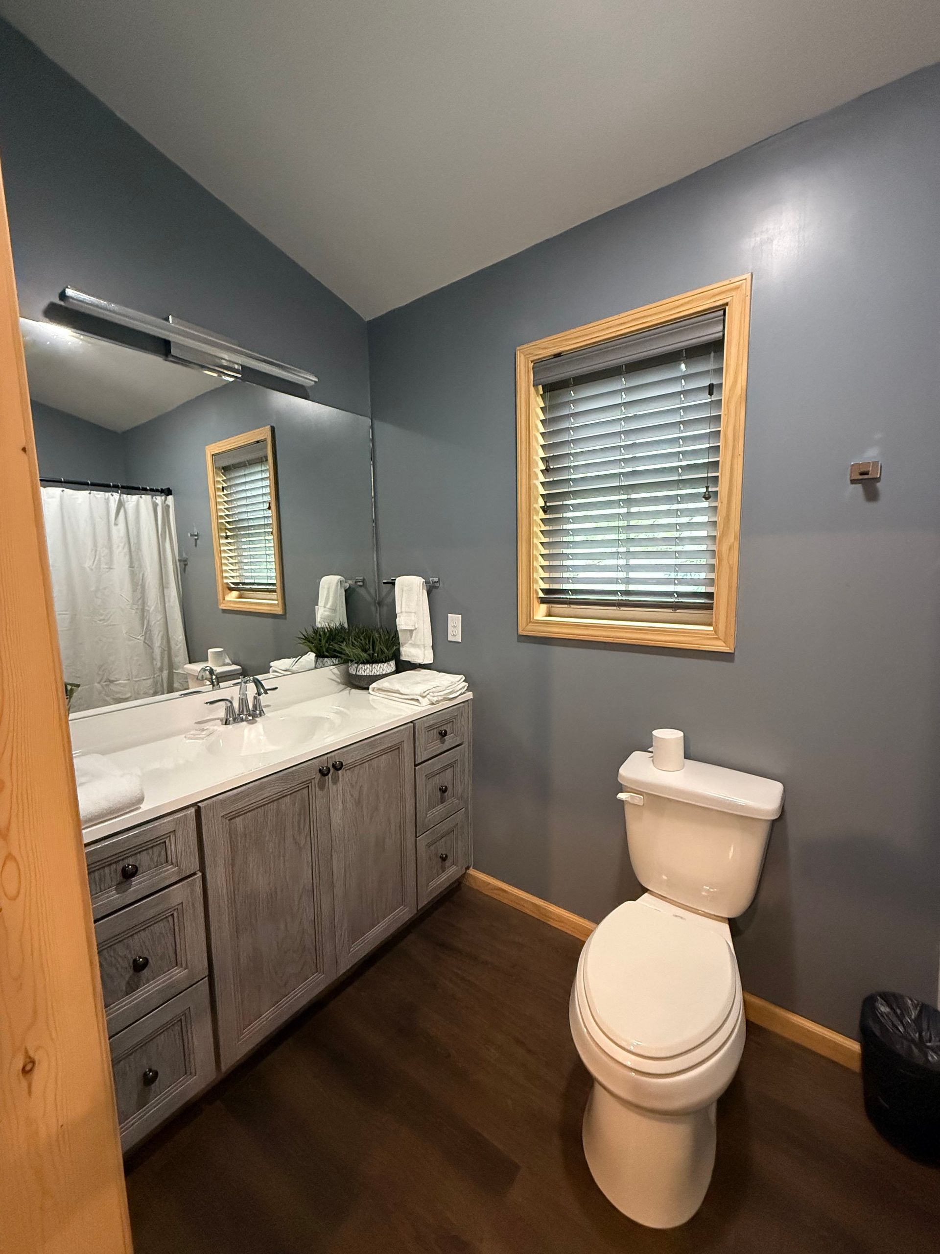 A bathroom with a toilet , sink , mirror and window.