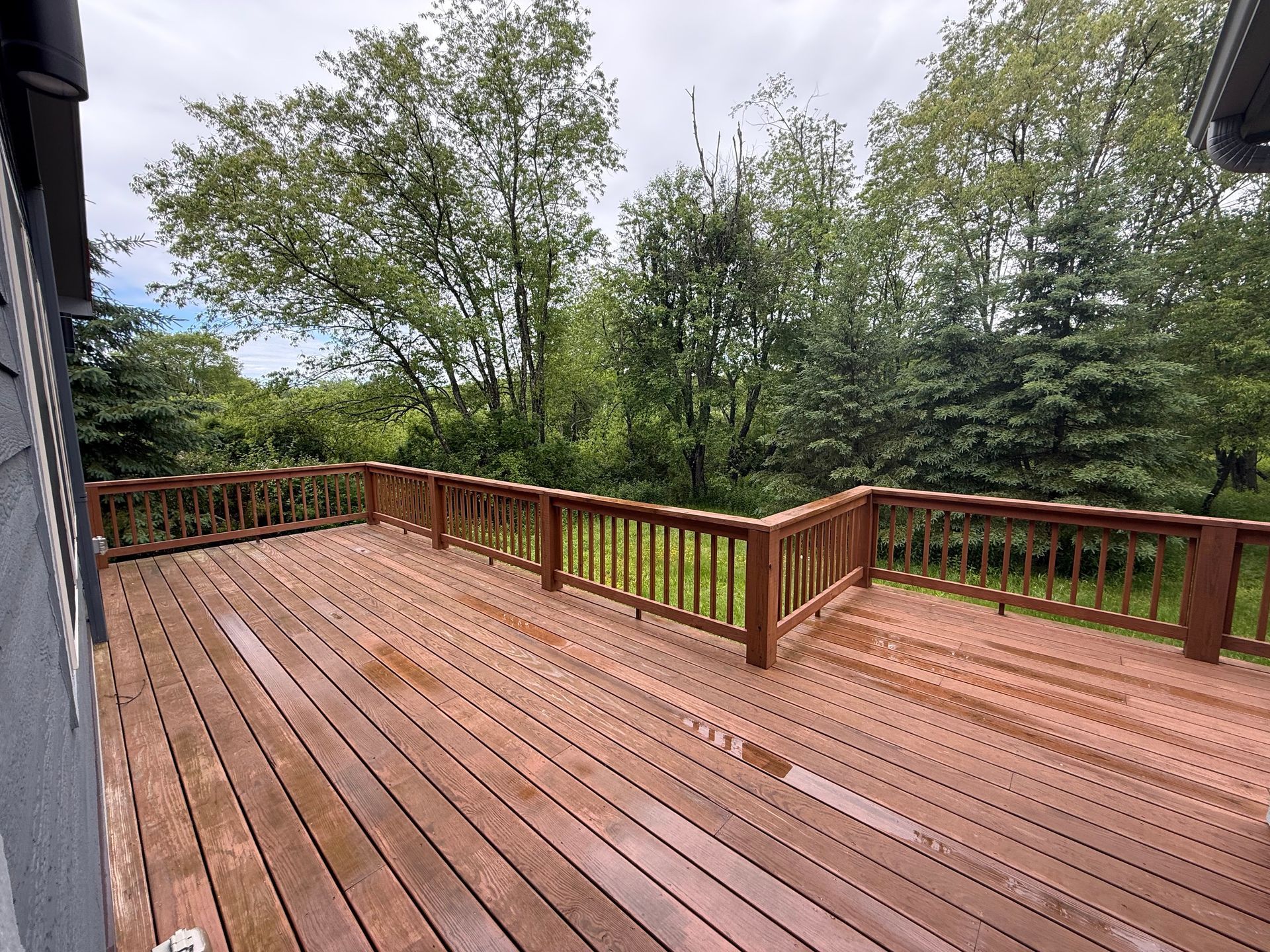 A large wooden deck with a railing and trees in the background.