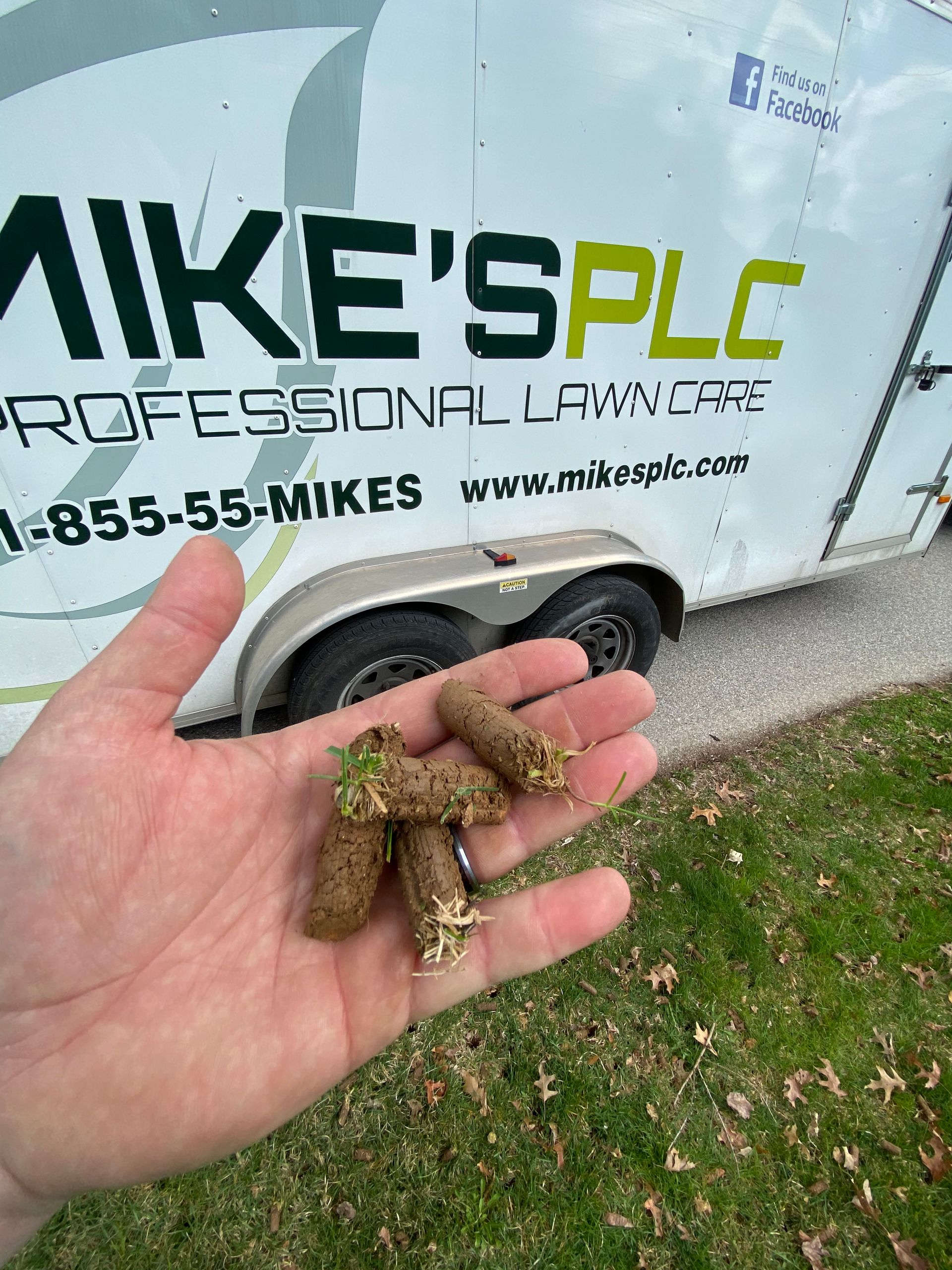 A person is holding a pile of grass in their hand in front of a trailer.